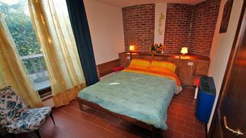 Un dormitorio con cama, dos lámparas de noche, una silla, una ventana con cortinas y una pared de ladrillo.