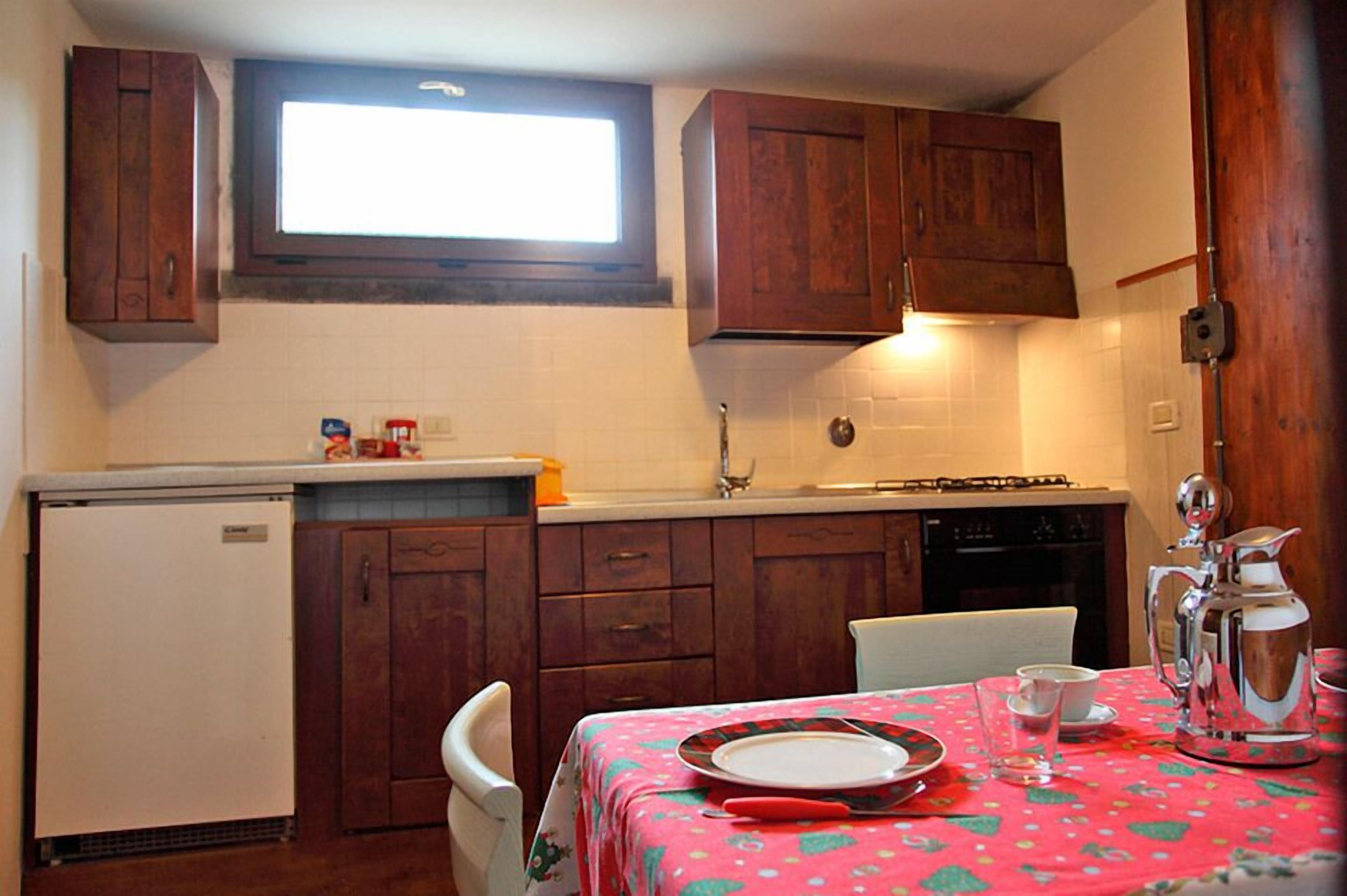 Una cocina compacta con armarios de madera, un refrigerador pequeño y una mesa de comedor preparada para dos.