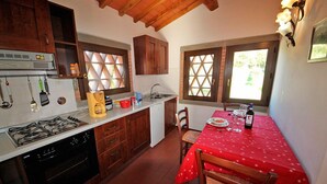 Una cocina con armarios de madera, una estufa a gas, un lavabo y una zona de comedor con mantel rojo.