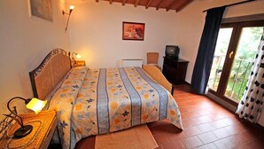 Un dormitorio con cama, escritorio con lámpara, televisor y ventana con cortinas.