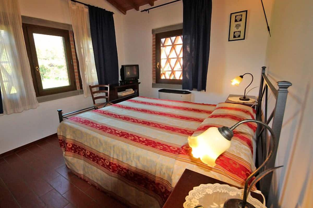 Ein Schlafzimmer mit einem Bett, einem Fernseher, einem Schreibtisch und einem Fenster mit Vorhängen.