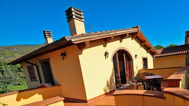 Un edificio con fachada amarilla, techo de tejas y un pequeño patio con una mesa y sillas.