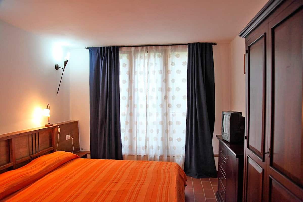 Ein Hotelzimmer mit einem Bett, einem Fernseher auf einer Kommode, einer Lampe und einem Fenster mit Vorhängen.