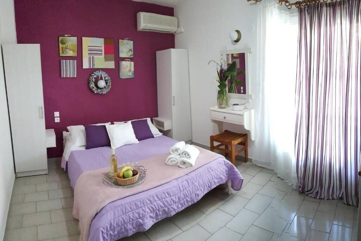 Un dormitorio con edredón morado, un escritorio con espejo y una ventana con cortinas.