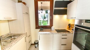 Cozinha compacta com pia, fogão e janela com vista para o verde.