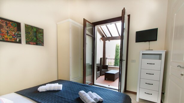 Quarto com cama, televisão, guarda-roupa e varanda com mobiliário.