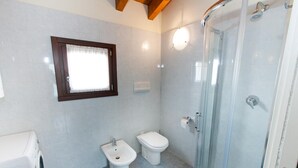 Casa de banho com cabine de duche em vidro, duas sanitas, um bidé e uma máquina de lavar roupa.