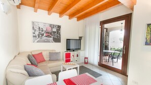 Sala de estar com sofá, televisão, mesinha e varanda com mobiliário de exterior.