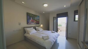 Ein modernes Schlafzimmer mit einem großen Bett, einem Gemälde an der Wand und einer Schiebetür zu einem Außenbereich.