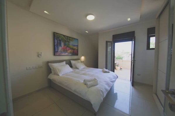 A modern bedroom with a large bed, a painting on the wall, and a sliding door leading to an outdoor area.