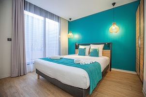 Cama bem arrumada com um manta verde-água, cabeceira de madeira e duas luminárias pendentes.