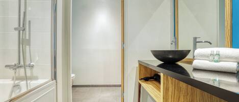 A modern bathroom with a glass-enclosed shower, a wooden vanity with a black basin, and a large mirror.