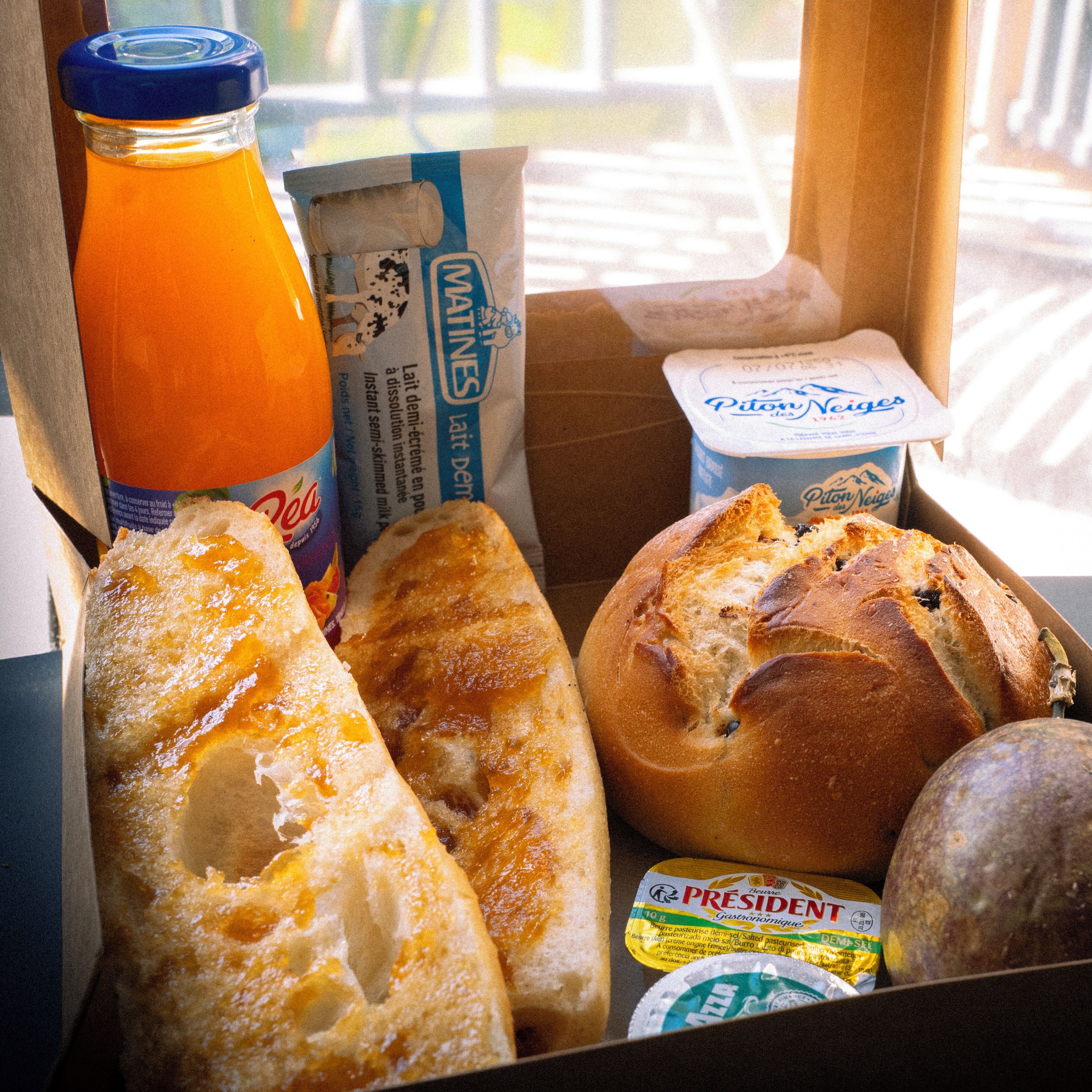 Una caja con diversos alimentos, como pan, una botella de jugo de naranja y productos lácteos.