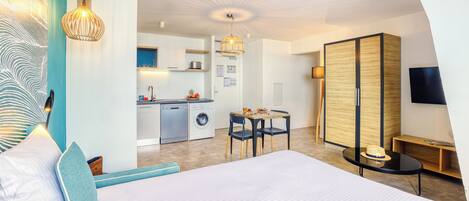 Una habitación de hotel moderna con una cama grande, una zona de comedor, una cocina y un televisor.