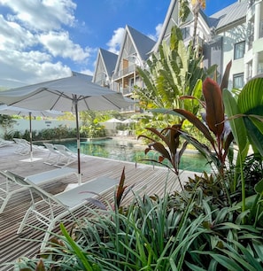 A poolside area with lounge chairs and umbrellas, surrounded by lush tropical plants.