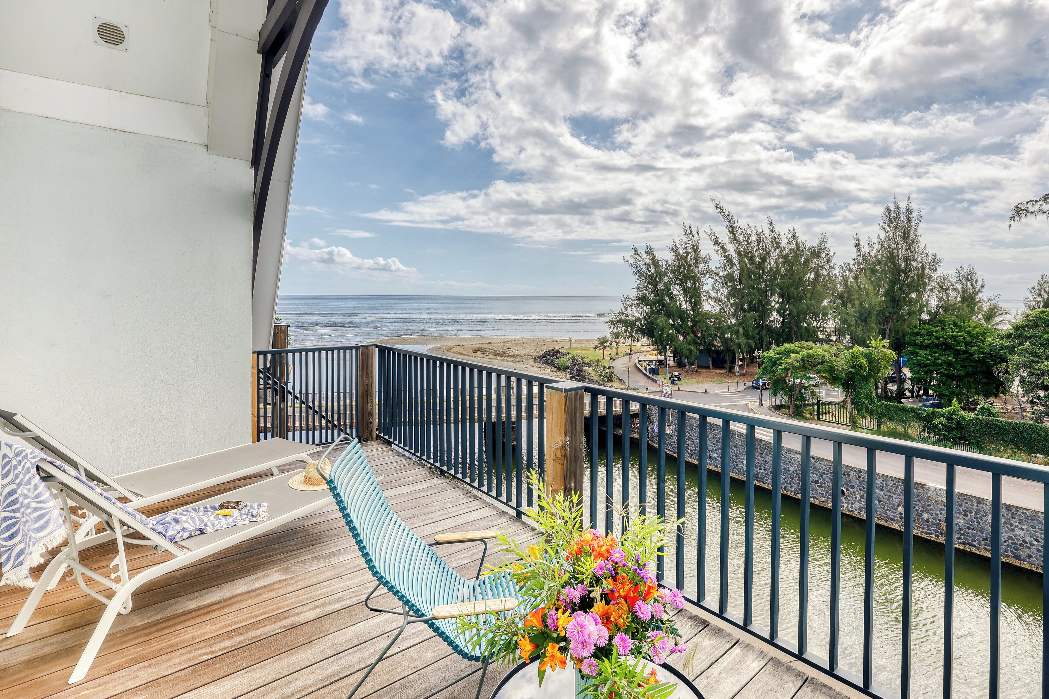 A balcony with a view of the sea, a wooden deck, and a flower arrangement.