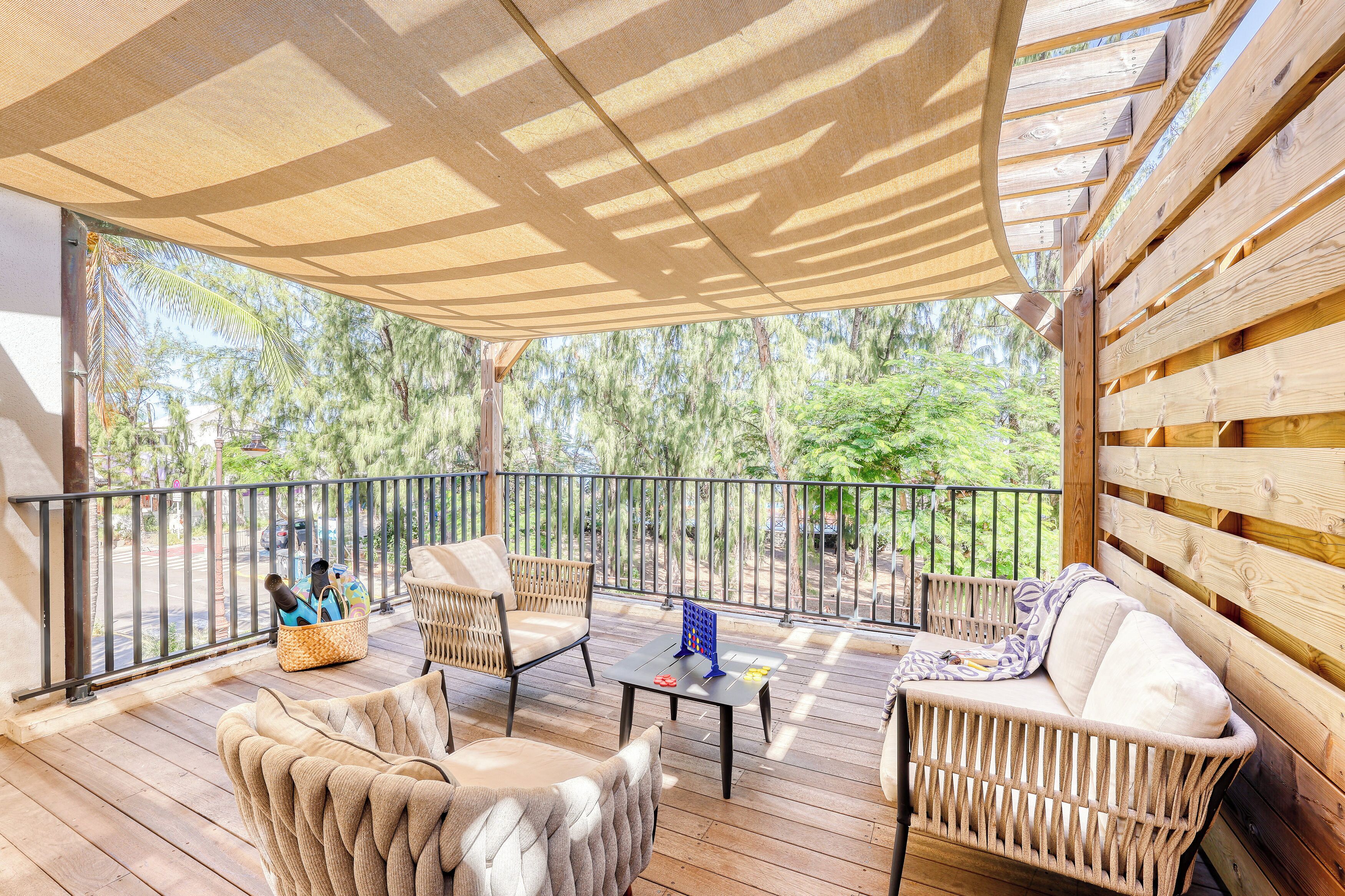 A wooden deck with wicker furniture, a shaded area, and a view of trees.