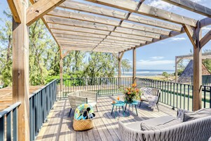 Um deck de madeira com móveis de exterior, uma pérgula e vista para o oceano.