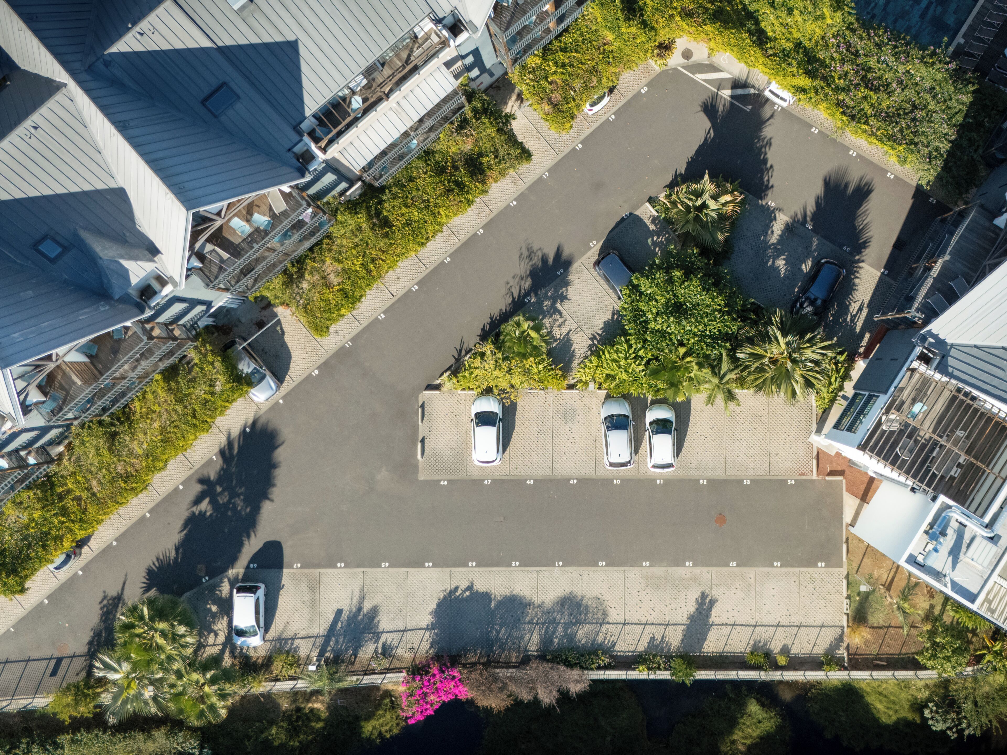 An aerial view of a residential area with a parking lot, numbered parking spaces, and surrounding greenery.