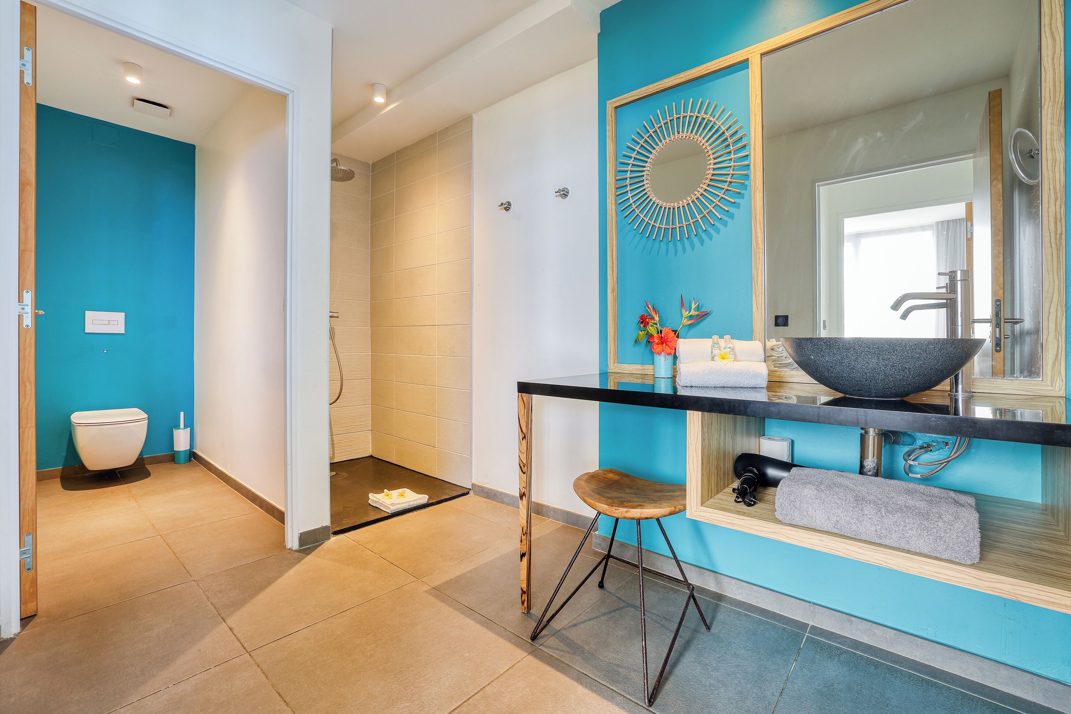 Une salle de bain moderne avec un mur d’accent bleu, un grand miroir, un lavabo noir et un espace douche.