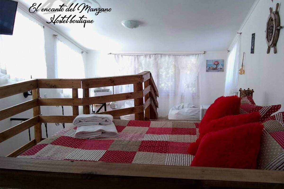 Un dormitorio con una cama litera de madera, un edredón a cuadros y almohadas rojas.