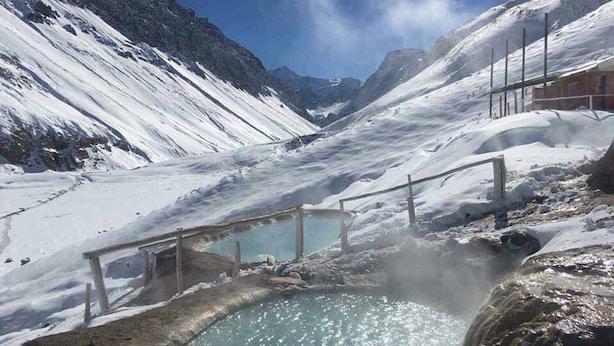 Un paysage montagneux enneigé avec une zone de sources chaudes comprenant un banc en bois et une petite piscine.