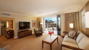 Un salon d’hôtel équipé d’une télévision, d’un canapé, d’une table basse et offrant une vue sur la ville grâce à de grandes fenêtres.