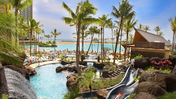 Un complexe hôtelier doté d’une piscine, de palmiers, d’une plage et d’un toboggan aquatique.