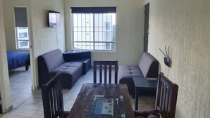 Ein Wohnzimmer mit Holztisch, zwei Sofas, einem an der Wand befestigten Fernseher und einem großen Fenster.