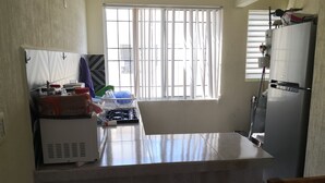 Eine Küche mit einem Gasherd, einem Kühlschrank, einem Fenster mit Jalousien und einem Stuhl.