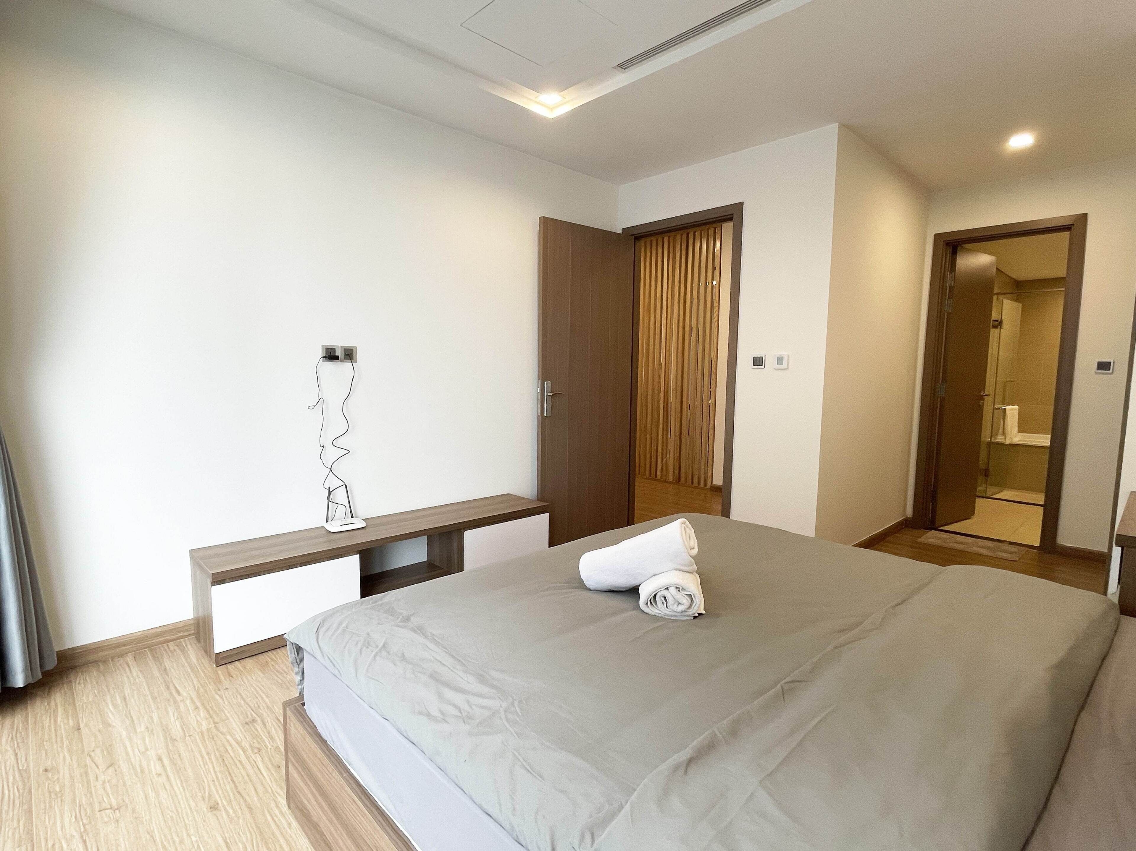 A modern bedroom with a bed, bedside tables, a wardrobe, and a bathroom visible through an open door.