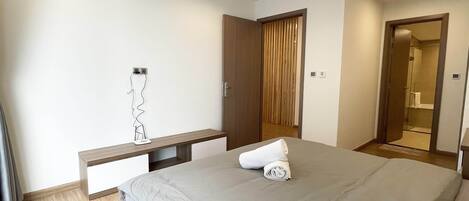 A modern bedroom with a bed, bedside tables, a wardrobe, and a bathroom visible through an open door.