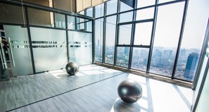 A modern interior with large windows offering a city view, a glass partition, and a metallic exercise ball.