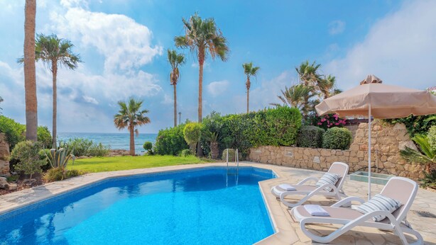 A swimming pool with lounge chairs and a stone wall. - Resitour - Apollo Beach Villas (Chlorakas)