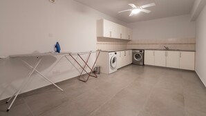 A modern kitchen with a washing machine, a ceiling fan, and a drying rack. - Resitour - Apollo Beach Villas (Chlorakas)