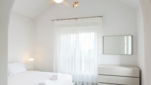 A minimalist bedroom with a bed, bedside table, and a ceiling fan. - Resitour - Apollo Beach Villas (Chlorakas)