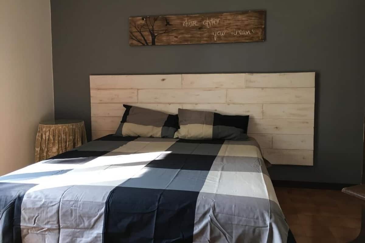 A bedroom with a wooden headboard, a checkered bedspread, and a motivational quote on the wall.