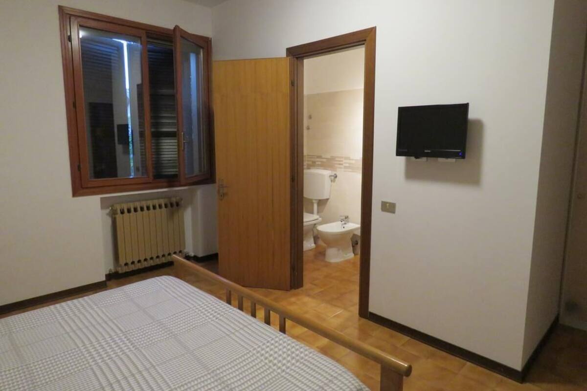 A bedroom with a bed, a wooden door, a radiator, and a television on the wall.