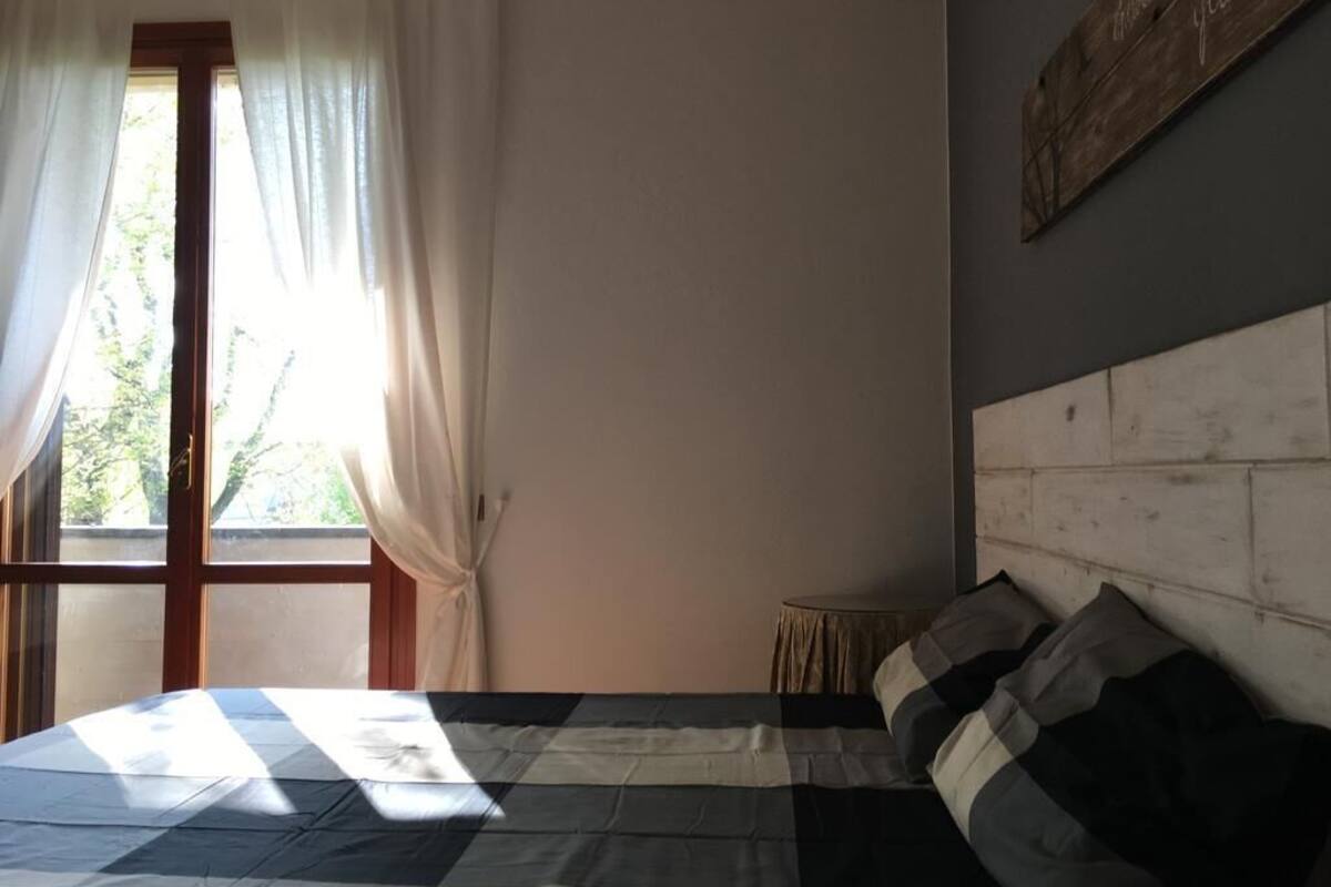 A bedroom with a bed, a window with curtains, a small round table, and a wooden headboard.
