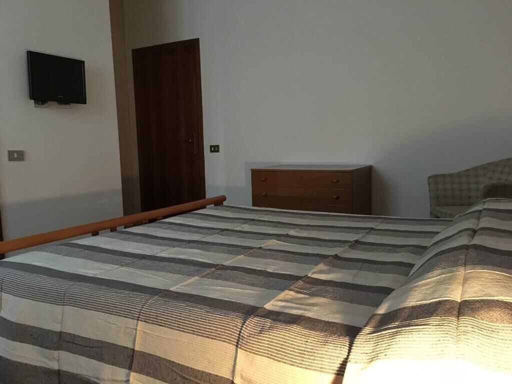 Ein Schlafzimmer mit einem Bett, einer Holzkommode, einem an der Wand befestigten Fernseher und einer Tür.