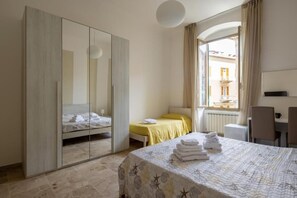 A hotel room with a bed, a wardrobe, a desk, and a window with a view of buildings.