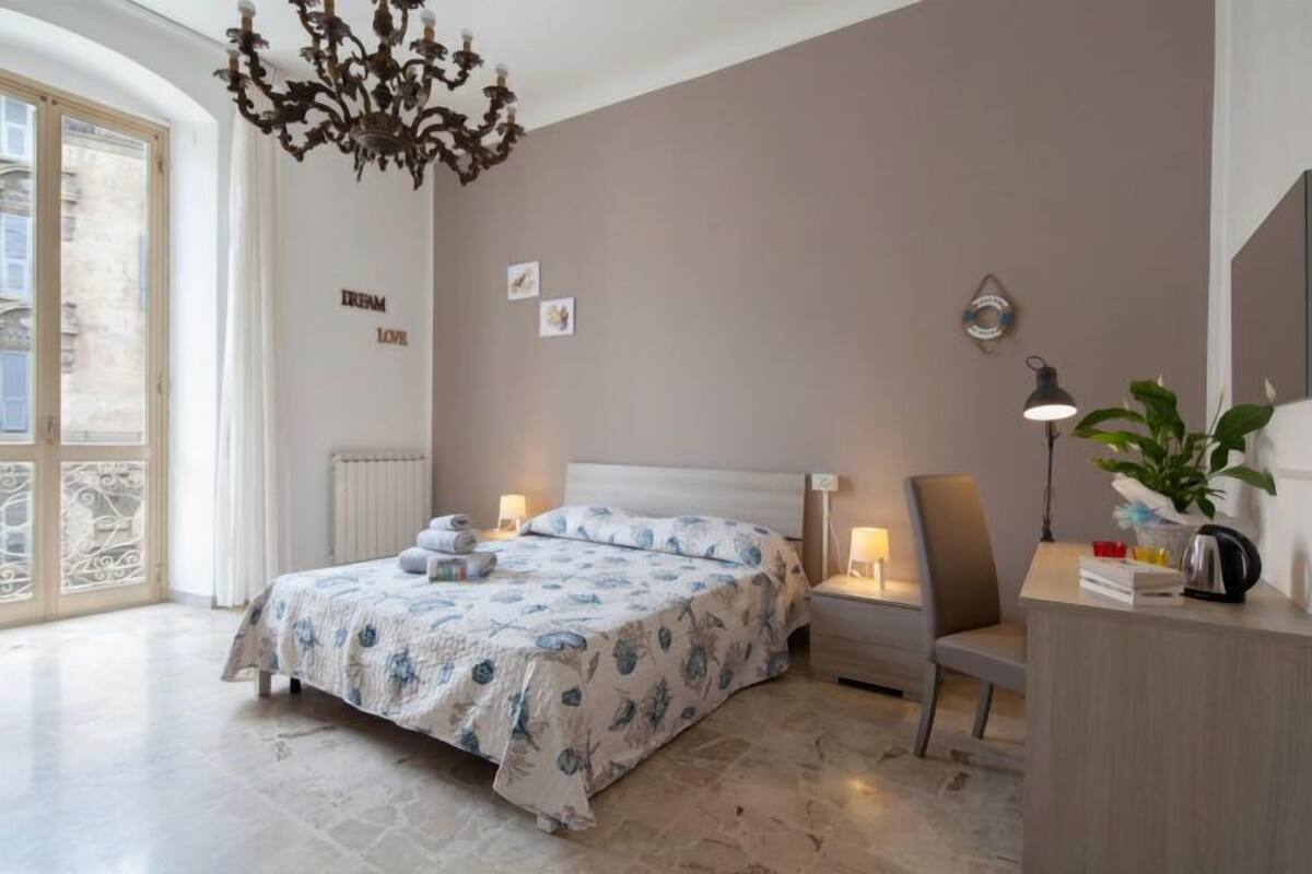 Een slaapkamer met een bed, nachtlampjes, een bureau en een plant.