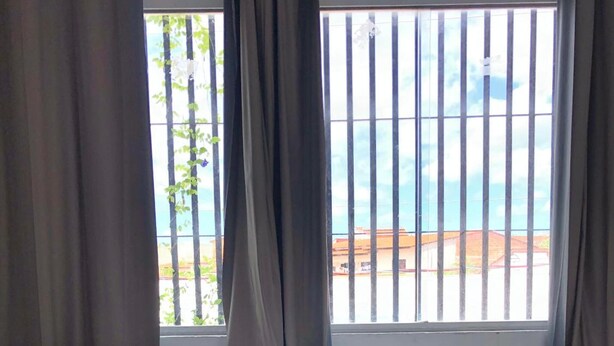 Une chambre d’hôtel avec un lit, deux oreillers, une couverture bleue et une vue sur la mer par une fenêtre équipée de stores verticaux.