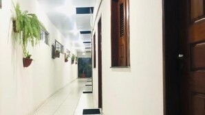 Un couloir avec un sol carrelé de carreaux blancs, des plantes en pot et une porte en bois.