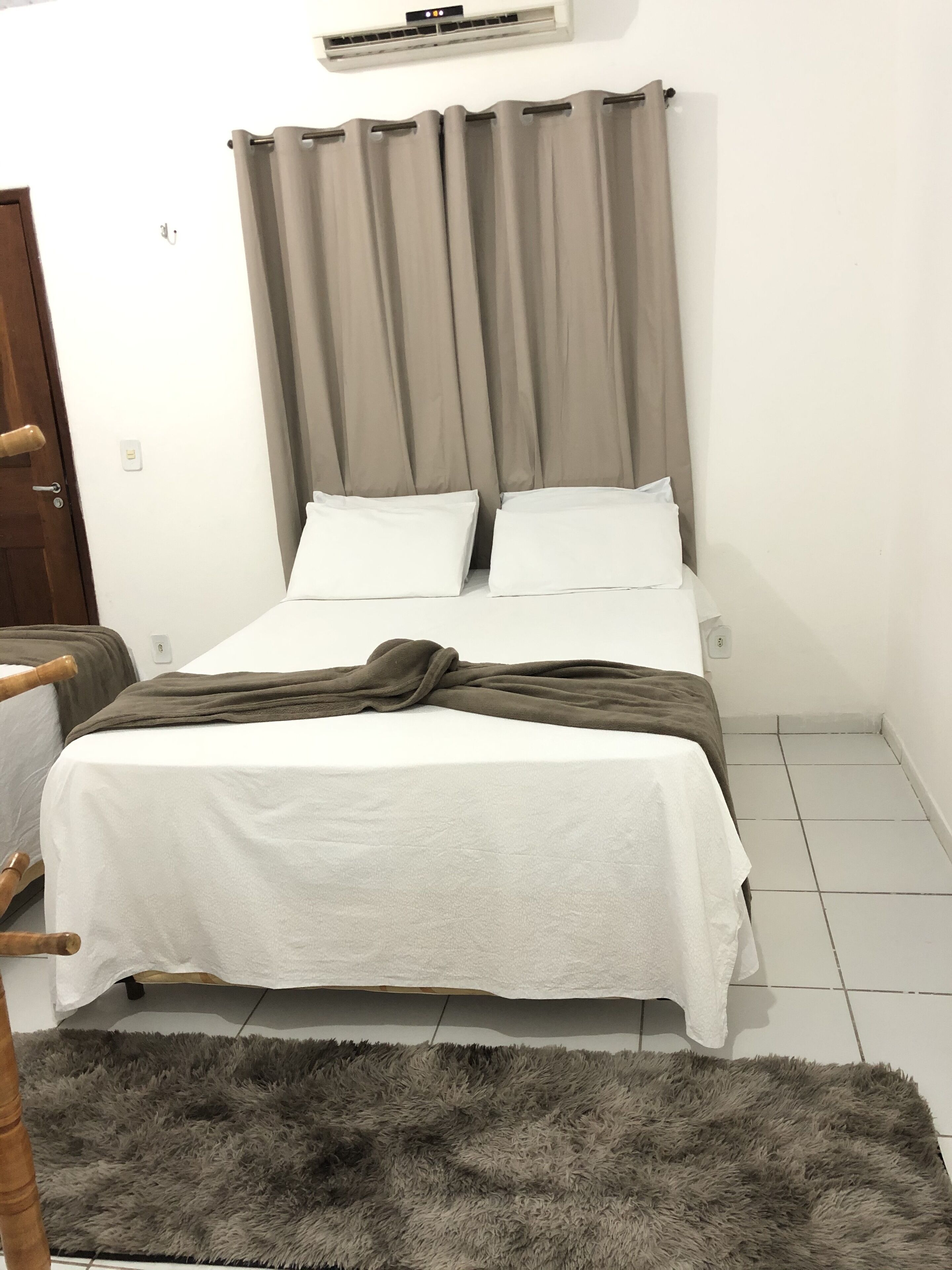 A bedroom with a bed, curtains, a wooden door, and a fluffy rug.