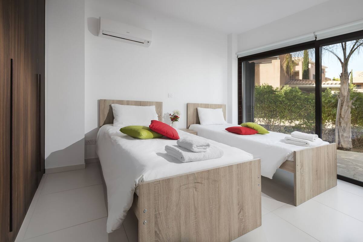 Una habitación de hotel moderna con dos camas de madera, sábanas blancas y almohadas de colores.