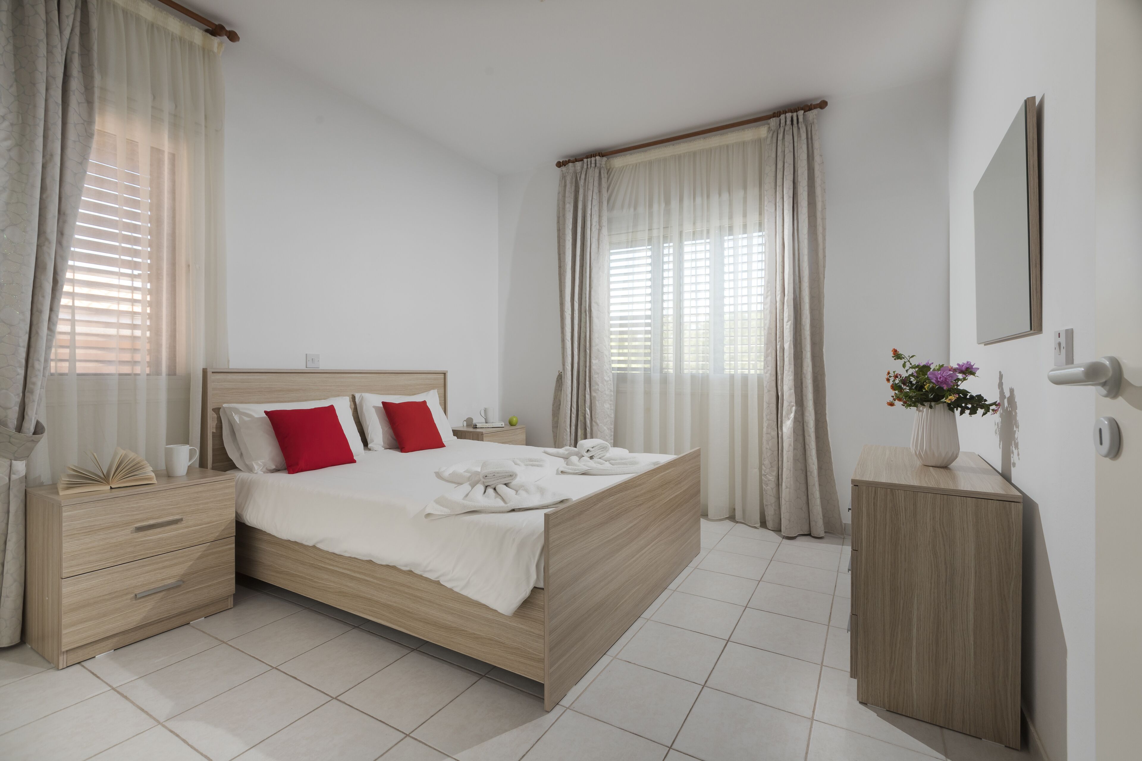 A neatly arranged bedroom with a wooden bed, a bedside table, a nightstand, and a small cabinet.