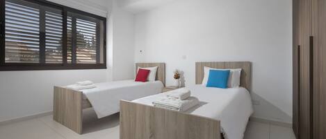 A modern bedroom with two beds, each with a wooden headboard, white bedding, and a small bedside table with a vase.