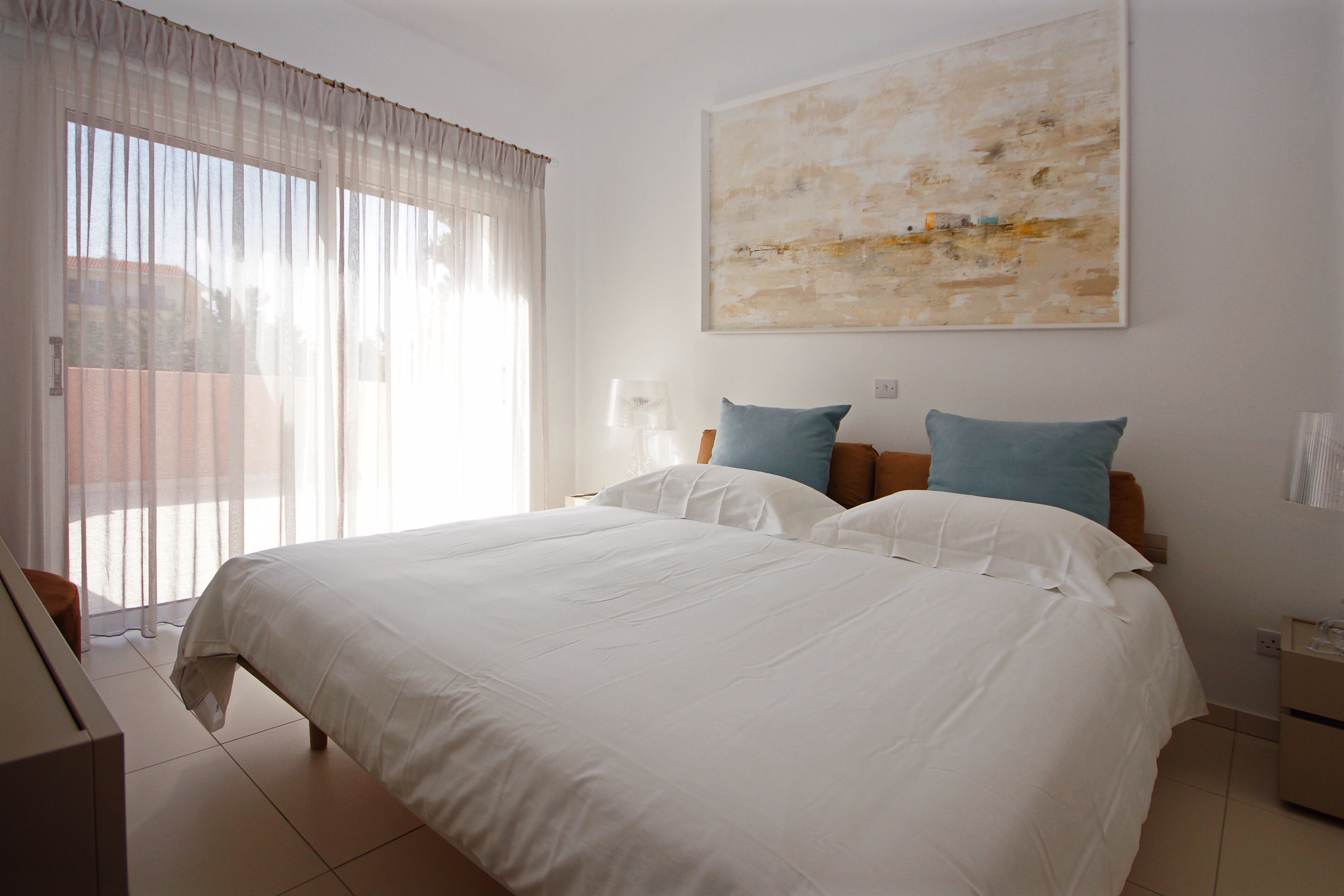 Une chambre d’hôtel avec un grand lit, deux oreillers, une table de chevet, une lampe et un grand tableau abstrait accroché au mur.