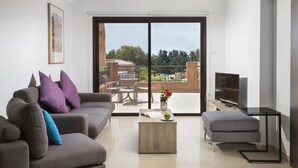 A modern living room with a grey sofa, a coffee table, and a TV. - Resitour - Aphrodite Gardens (Paphos)
